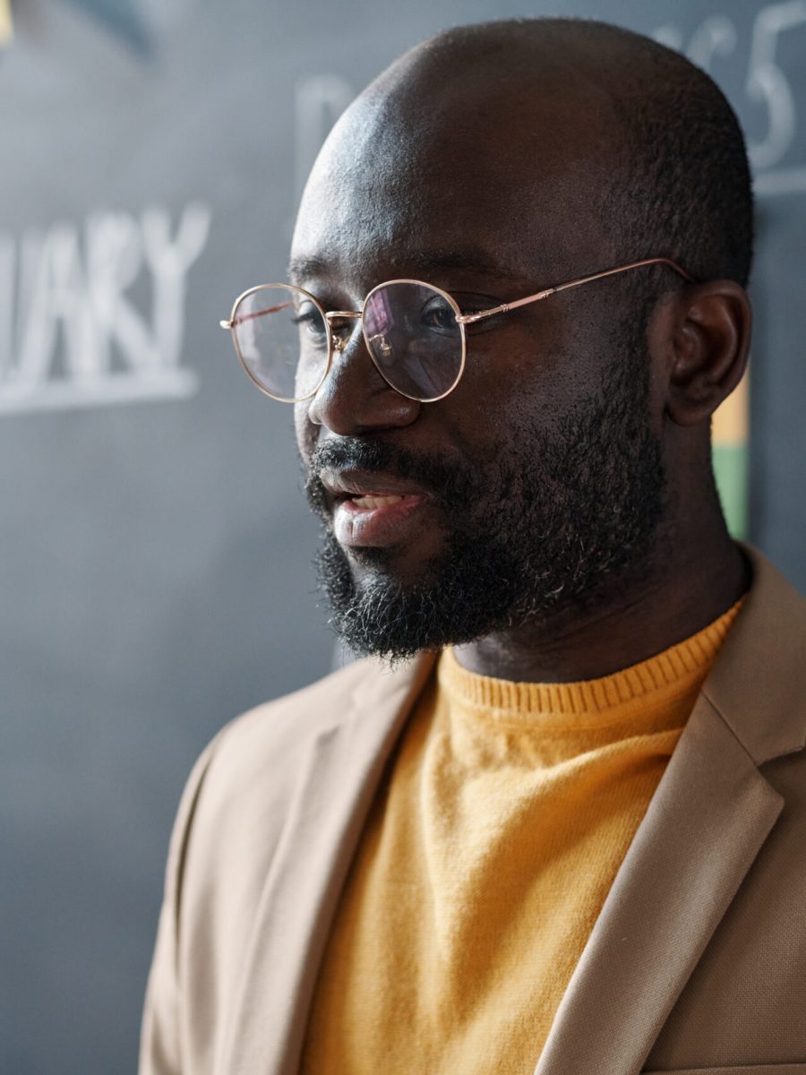 Close-up of African American teacher in eyeglasses talking at lecture against blackboard