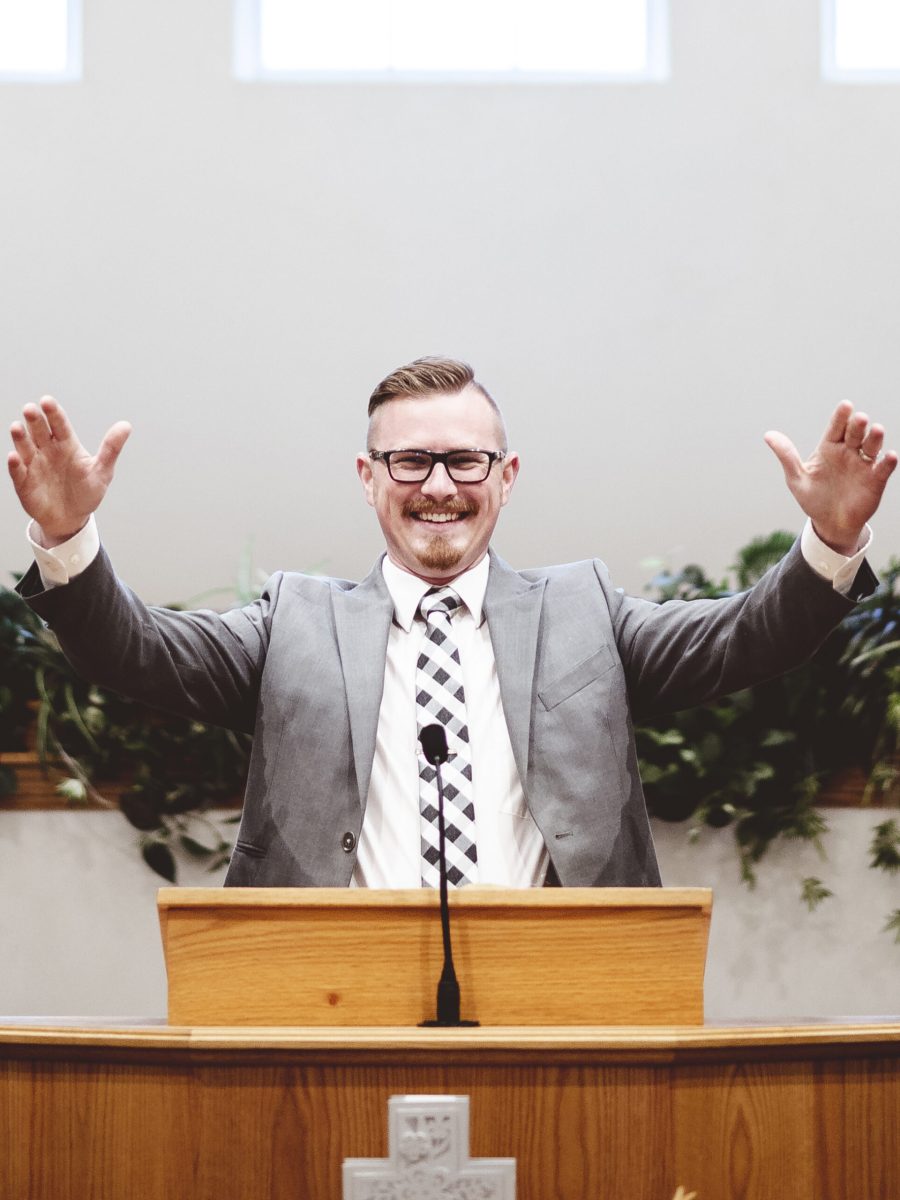A vertical shot of a male in a suit preaching words of the Holy Bible at the altar of a church